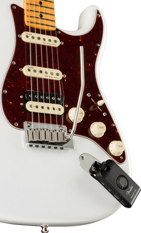 The image shows a Fender Stratocaster electric guitar with a white body, burgundy tortoiseshell pickguard, maple neck, and three single-coil pickups (two cream, one black). It features a chrome tremolo bridge, three control knobs, and standard Stratocaster electronics. Attached is a black Fender wireless transmitter, enabling cable-free play, blending classic design with modern wireless functionality for live performance.