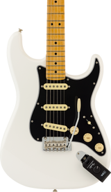 The image shows a classic white/cream Fender Stratocaster-style electric guitar with a maple neck and fretboard. It features a black pickguard, three cream single-coil pickups, chrome bridge and tuning pegs, cream control knobs, and a 5-way selector switch. Standard fret markers and six strings are visible. A small black device is in the lower right corner. The guitar displays the iconic Stratocaster body shape and hardware.