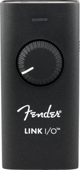 The image shows a Fender Link I/O, a compact black audio interface with a speckled finish, featuring a large central rotary knob, a small top button, Fender branding, and a USB port. It connects guitars and electric instruments to computers or mobile devices for recording, practicing, and live use, enabling digital audio input for musicians and producers.