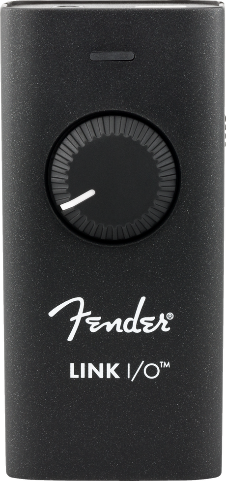 The image shows a Fender Link I/O, a compact black audio interface with a speckled finish, featuring a large central rotary knob, a small top button, Fender branding, and a USB port. It connects guitars and electric instruments to computers or mobile devices for recording, practicing, and live use, enabling digital audio input for musicians and producers.