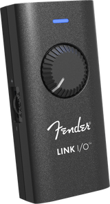 The image shows a Fender LINK I/O audio interface, a compact, portable device for connecting guitars or basses to computers, tablets, or smartphones. It features a black textured housing with the white Fender logo, a large central rotary knob, a blue LED indicator, and multiple side ports for inputs and outputs. Designed for recording, practice, and music production, it enables seamless integration with digital audio workstations and amp simulation software.
