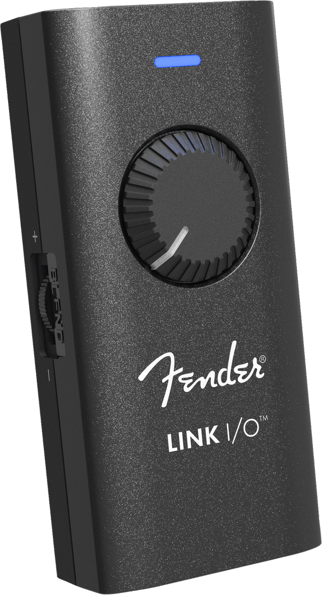 The image shows a Fender LINK I/O audio interface, a compact, portable device for connecting guitars or basses to computers, tablets, or smartphones. It features a black textured housing with the white Fender logo, a large central rotary knob, a blue LED indicator, and multiple side ports for inputs and outputs. Designed for recording, practice, and music production, it enables seamless integration with digital audio workstations and amp simulation software.
