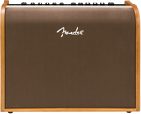 The image shows a Fender acoustic guitar amplifier with a wood-grain finish on the sides and a brown/bronze front grille. The white Fender logo is displayed on the front. Along the top edge are control knobs for volume and EQ. This medium-sized combo amp is designed to amplify acoustic guitars, delivering natural, warm sound, making it suitable for practice, small venues, or recording.