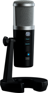 The image shows a professional USB condenser microphone with a large diaphragm and metal mesh grille. It has a black cylindrical body with silver accents, built-in desktop stand, and controls including preset and monitor buttons, a volume knob with blue LED, push-to-mute, and a headphone jack. Ideal for vocals, instruments, podcasting, and streaming, it offers high-quality, plug-and-play recording for musicians and content creators.