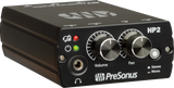 The image shows a PreSonus HP2 headphone amplifier, a compact black unit used in studios for headphone distribution. Visible features include a headphone jack, volume and pan knobs, stereo/mono switch, power and mute buttons, and red/green LED indicators. It allows multiple users to monitor audio with individual volume and stereo control by connecting to mixers or audio interfaces.