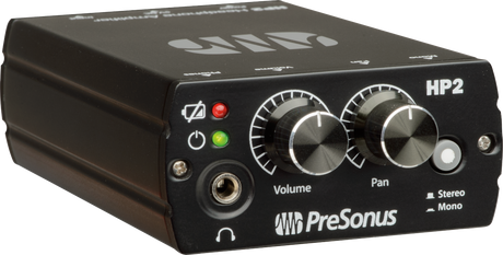 The image shows a PreSonus HP2 headphone amplifier, a compact black unit used in studios for headphone distribution. Visible features include a headphone jack, volume and pan knobs, stereo/mono switch, power and mute buttons, and red/green LED indicators. It allows multiple users to monitor audio with individual volume and stereo control by connecting to mixers or audio interfaces.