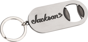 The image shows a metal keychain bottle opener branded with the Jackson logo, a well-known electric guitar manufacturer popular in rock and metal music. This promotional merchandise item highlights Jackson’s identity within the guitar industry, where they produce accessories alongside their high-performance guitars like the Soloist, Dinky, and Rhoads models.