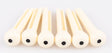 The image shows six light-colored wooden reeds, likely for woodwind instruments like clarinets or oboes, arranged in a row against a white background. Each reed is flat, thin, and rounded at one end, featuring small dark holes. The natural wood grain is visible. These reeds are essential, consumable parts for woodwind players, regularly replaced to maintain sound quality and playability.