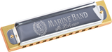 The image shows a Hohner Marine Band harmonica with a traditional wooden comb, gray/silver cover plates featuring the "MARINE BAND" text, the Hohner logo with a portrait, and "M. Hohner" script. It has a classic diatonic design with visible reed chambers. The harmonica, popular since 1896 among blues, folk, and country musicians, is photographed against a white background.
