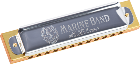 The image shows a Hohner Marine Band harmonica with a traditional wooden comb, gray/silver cover plates featuring the "MARINE BAND" text, the Hohner logo with a portrait, and "M. Hohner" script. It has a classic diatonic design with visible reed chambers. The harmonica, popular since 1896 among blues, folk, and country musicians, is photographed against a white background.