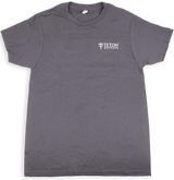 The image shows a gray t-shirt with the "Teton Guitars" logo printed in white on the chest. This branded apparel is merchandise from Teton Guitars, a company known for producing acoustic guitars. The shirt likely serves as promotional or fan gear, representing the type of merchandise musical instrument manufacturers create to promote their brand and generate additional revenue.