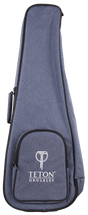 The image shows a TETON Music ukulele gig bag made of blue denim-like fabric with black trim. It features the "TETON UKULELES" logo on the front zippered pocket. The padded soft case includes a main compartment for a ukulele, accessory storage, carrying handles, shoulder strap capability, and a full-length zipper for easy access, offering stylish, practical protection for the instrument.