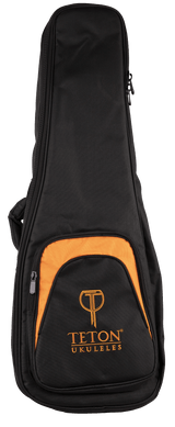 The image shows a TETON ukulele gig bag in black with orange accents. It features padded protection, multiple zippered compartments including a front pocket with the "TETON UKULELES" logo, and side carrying handles. Sized for concert or tenor ukuleles, this soft case offers secure transport and storage for the instrument and accessories like picks and tuners.