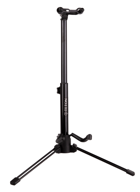 The image shows a black professional-grade tripod guitar stand with an adjustable central pole, three folding legs for stability, an upper cradle for the guitar neck, and a lower arm to support the body. The brand "DELTON" is visible on the pole. This sturdy, height-adjustable stand is used by guitarists to securely display and store acoustic or electric guitars in studios, on stage, or at home.