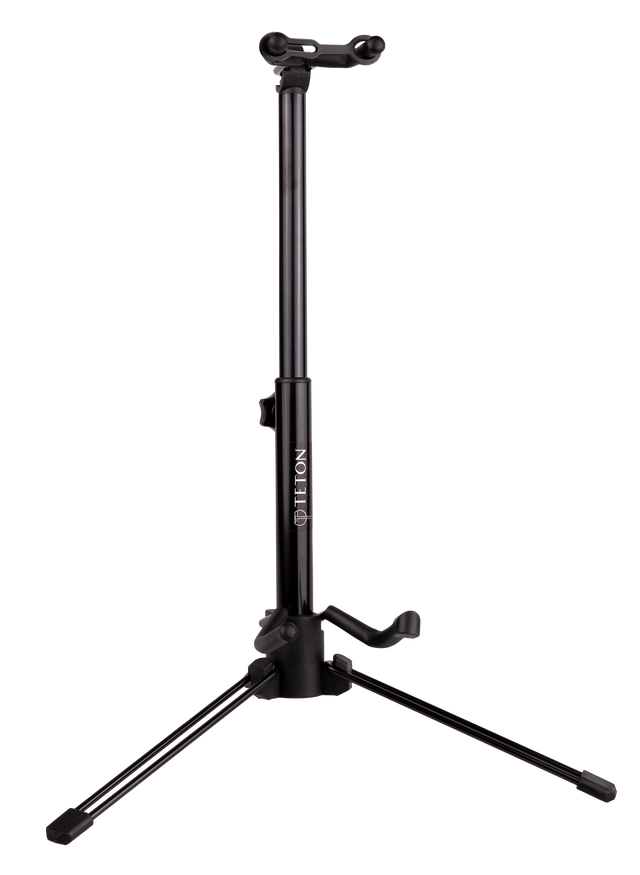 The image shows a black professional-grade tripod guitar stand with an adjustable central pole, three folding legs for stability, an upper cradle for the guitar neck, and a lower arm to support the body. The brand "DELTON" is visible on the pole. This sturdy, height-adjustable stand is used by guitarists to securely display and store acoustic or electric guitars in studios, on stage, or at home.
