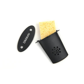 The image shows a D'Addario instrument humidifier with a black plastic housing, ventilation holes, a yellow sponge insert, and branded oval cover. It has a clip for securing inside acoustic guitars and other wooden stringed instruments. Designed to maintain proper humidity (45-55%), it prevents wood from drying, cracking, and damage, helping preserve the instrument's structure and sound quality.