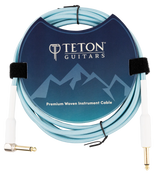 The image shows a Teton Guitars Premium Woven Instrument Cable with a light blue woven exterior for durability. It features gold-plated 1/4" TS connectors—one straight and one right-angle—and includes Velcro ties for organization. The cable is neatly coiled and displayed in professional packaging with Teton Guitars branding, designed for connecting electric guitars or basses to amplifiers or audio gear.