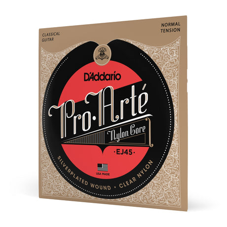 The image shows a package of D'Addario Pro-Arté EJ45 classical guitar strings. These nylon core, normal tension strings feature silver-plated wound basses and clear nylon trebles. The packaging has a tan background with decorative scrollwork and a central black and red logo. Made in the USA, this popular premium set offers warm tone and reliable intonation, suitable for students and professionals alike.
