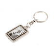 The image shows a music-themed keychain with a rectangular metal frame containing a black-and-white photo, likely of a musician or band. It is attached to a metal keyring by a chain link. This merchandise item is typical for music fans to show support and is commonly sold at music stores, concert venues, and online shops alongside other fan accessories.