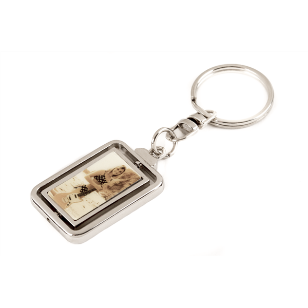 The image shows a silver-toned metal keychain with a rectangular pendant featuring a music-themed design, possibly musical notes or sheet music. It has a standard key ring attachment and combines practicality with musical decoration. This accessory is popular among musicians, students, and music lovers as a functional item that expresses their passion for music.