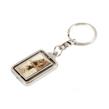 The image shows a silver-toned metal keychain with a rectangular pendant featuring a music-themed design, possibly musical notes or sheet music. It has a standard key ring attachment and combines practicality with musical decoration. This accessory is popular among musicians, students, and music lovers as a functional item that expresses their passion for music.