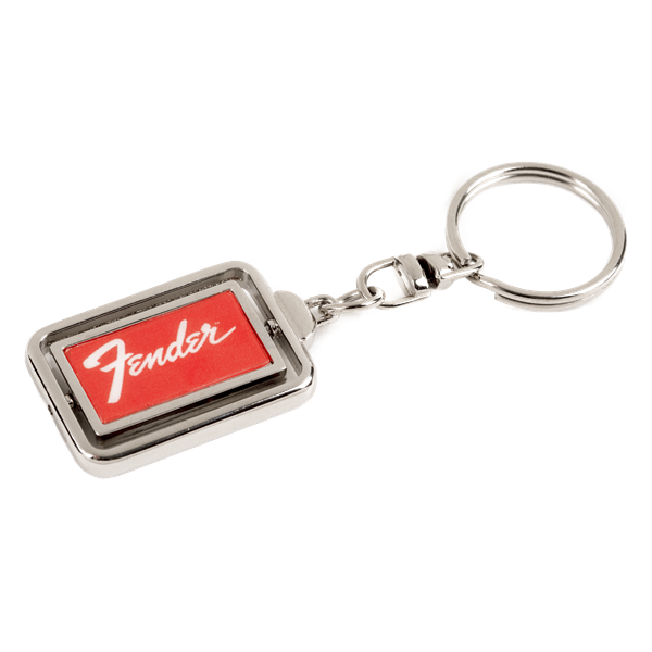 The image shows a metal Fender keychain with a rectangular design featuring the red Fender logo on a dark background, framed by chrome-colored metal. It includes a standard key ring attached by a small chain link. This branded accessory represents Fender, a renowned guitar and amplifier manufacturer popular among musicians and fans.