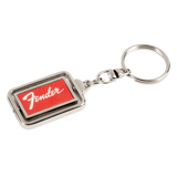 The image shows a metal Fender keychain with a rectangular design featuring the red Fender logo on a dark background, framed by chrome-colored metal. It includes a standard key ring attached by a small chain link. This branded accessory represents Fender, a renowned guitar and amplifier manufacturer popular among musicians and fans.