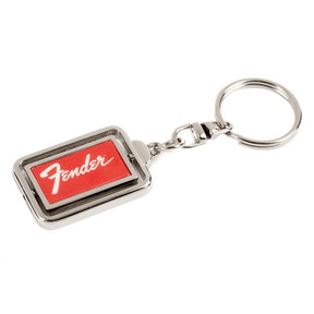 The image shows a metal Fender keychain with a rectangular design featuring the red Fender logo on a dark background, framed by chrome-colored metal. It includes a standard key ring attached by a small chain link. This branded accessory represents Fender, a renowned guitar and amplifier manufacturer popular among musicians and fans.