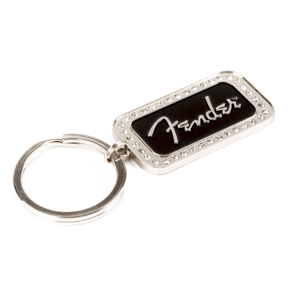 The image shows a Fender keychain featuring a rectangular metal charm with a black center displaying the white Fender logo in signature script. The charm has a decorative beaded border and is attached to a standard split-ring. This music-themed accessory is popular among musicians and fans as a collectible or gift, representing the iconic brand known for electric guitars and amplifiers.