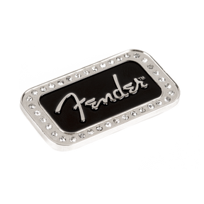The image shows a Fender logo magnet, a decorative metal emblem featuring the iconic silver "Fender" script on a black background. It is bordered by small rhinestones.
