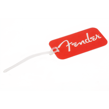The image shows a bright red rectangular Fender luggage tag featuring the white Fender logo and script. It has a clear plastic loop for attaching to luggage or instrument cases. This branded accessory is designed for musicians to identify their gear while traveling and serves as practical merchandise for Fender fans.