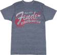 The image shows a heather gray Fender t-shirt featuring vintage-style graphics celebrating the iconic Fender Stratocaster guitar. The design includes "Since 1954," large "Fender" script, bold "STRATOCASTER" text, and a stylized guitar silhouette. This music merchandise appeals to fans and musicians, honoring one of the most influential electric guitars in history.