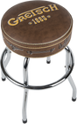 The image shows a Gretsch-branded bar stool with a round brown leather seat featuring the "Gretsch" logo and "1883" in gold lettering. It has chrome metal legs, decorative stitching, and small Gretsch logo details on the seat edges. This music-themed stool is branded merchandise designed for musicians or fans, typically used in studios or performance spaces to showcase the iconic Gretsch brand.