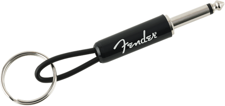 The image shows a Fender-branded keychain designed to look like a guitar cable. It features a 1/4" guitar plug on one end, a metal keyring on the other, and a black cable-like connector with the white Fender logo. This music-themed accessory mimics an instrument cable and is a novelty item for guitar players and Fender fans to carry keys while showing brand loyalty.