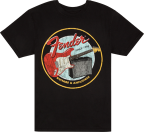 The image shows a black t-shirt with a vintage-style circular Fender logo. It features "Fender" in red script, "Since 1946," a red Stratocaster-style guitar, and a guitar amplifier. The bottom of the circle reads "GUITARS & AMPLIFIERS." This design highlights Fender's legacy as a leading maker of electric guitars and amplifiers.