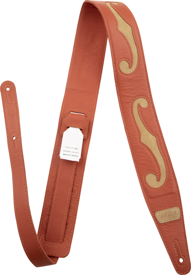 The image shows a high-quality leather guitar strap in rich brown/cognac with tan/cream decorative inlays forming a flowing, ornate pattern. It features detailed stitching, adjustable length with multiple holes, a small "GUITAR" brand label with "Made in Canada" marking, and professional hardware. This premium strap combines functionality with artisanal, handcrafted aesthetic appeal.