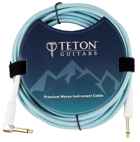 The image shows a Teton Guitars Premium Woven Instrument Cable with a light blue/turquoise woven jacket for durability and style. It has one straight and one right-angle 1/4" (6.35mm) gold-plated plug. The cable is coiled and secured with velcro, displayed in branded packaging featuring a mountain-themed design. This cable is ideal for connecting guitars, basses, and other instruments to audio gear, offering enhanced protection and signal quality.