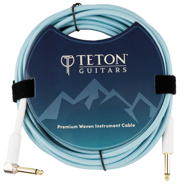 The image shows a Teton Guitars Premium Woven Instrument Cable with a light blue/turquoise woven jacket for durability and style. It has one straight and one right-angle 1/4" (6.35mm) gold-plated plug. The cable is coiled and secured with velcro, displayed in branded packaging featuring a mountain-themed design. This cable is ideal for connecting guitars, basses, and other instruments to audio gear, offering enhanced protection and signal quality.