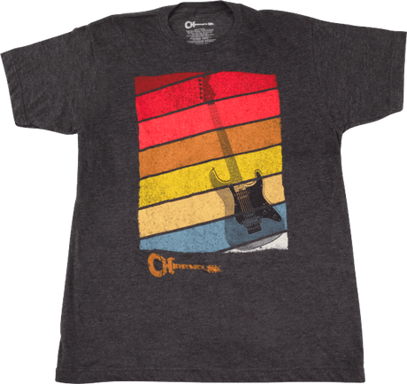 The image shows a dark gray t-shirt with a retro-style graphic of horizontal stripes in red, orange, yellow, and blue, resembling a vintage sunset. Silhouetted against the stripes is an electric guitar outline. Below the design is the "Charvel" logo, indicating official merchandise from the well-known guitar manufacturer popular in rock and metal music.
