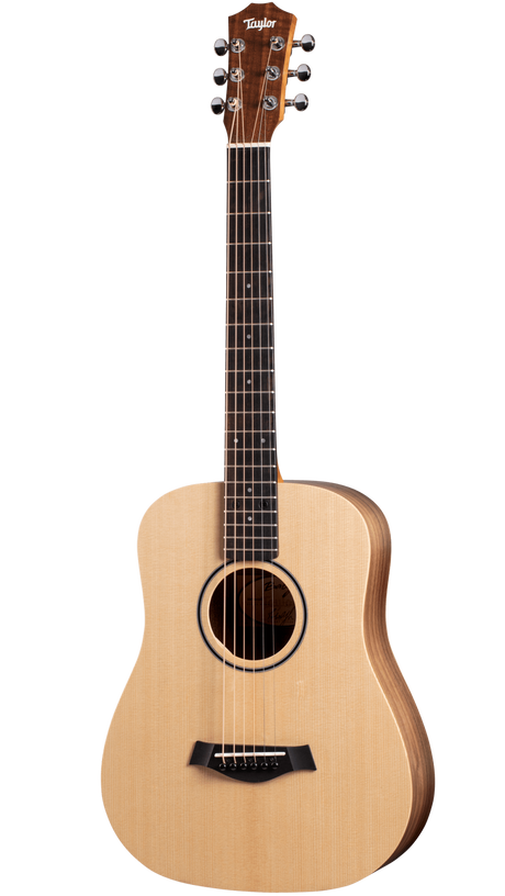The image shows a Taylor small-bodied acoustic guitar, likely from the Academy or entry-level series. It features a natural spruce top, darker wood back and sides, and a dark rosewood or ebony fretboard. Chrome tuning pegs (3+3), a black bridge, and a round soundhole with a dark rosette are visible. The guitar has a clean, simple design, suitable for beginners to intermediate players and various acoustic styles.