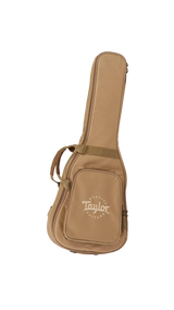 The image shows a tan Taylor guitar gig bag with the Taylor Guitars logo and "QUALITY GUITARS" text on the front pocket. This padded soft case features dual handles, shoulder straps, multiple compartments, and a full-length zipper. Made of durable material, it is designed to protect and transport acoustic guitars. Taylor is a well-known American guitar maker, and this lighter, portable gig bag is an accessory for their acoustic guitars.