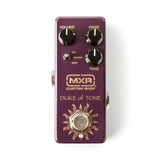 The image shows an MXR Custom Shop "Duke of Tone" overdrive/distortion guitar pedal in a purple/burgundy enclosure with gold lettering. It has three knobs: Volume (top left), Drive (top right), and Tone (bottom right), plus a toggle switch labeled "OD/BOOST/DIST" for selecting overdrive, boost, or distortion modes. The pedal features MXR’s compact design with a sun-like graphic around the footswitch and input/output jacks on the sides.