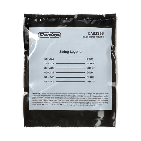 The image shows a package of Dunlop "String Legend" DAB1356 80/20 bronze acoustic guitar strings. It contains a full set of six medium-light gauge strings (.013-.056) with color-coded ball ends for identification: 1E (Gold), 2B (Black), 3G (Silver), 4D (Gold), 5A (Black), and 6E (Silver). The vacuum-sealed pack includes safety warnings and corrosion inhibitor technology to keep strings fresh.
