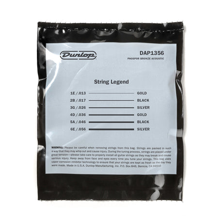 The image shows a package of Dunlop DAP1356 "String Legend" Phosphor Bronze acoustic guitar strings, medium-light gauge (13-56). The black sealed pack has a white label listing string gauges and colors: 1E/.013 (Gold), 2B/.017 (Black), 3G/.026 (Silver), 4D/.036 (Gold), 5A/.046 (Black), 6E/.056 (Silver). It includes safety info and features vapor corrosion inhibitor technology. Made by Dunlop in Benicia, California.