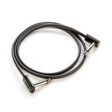 The image shows a short guitar patch cable with 1/4-inch TS right-angled connectors on both ends. It has a dark gray or black jacket and silver metal plugs. Commonly used to connect electric guitars, basses, keyboards, or pedals to amplifiers or audio gear, this compact cable is essential for clean, reliable signal routing in musical setups, especially on pedalboards.