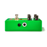 The image shows a compact, bright green guitar effects pedal with a metal chassis. It features four black control knobs, input and output jacks on the sides, a footswitch to engage or bypass the effect, and colorful graphics on the top panel. This mini stompbox is designed to modify guitar sound with effects like distortion or delay while saving space on a pedalboard.