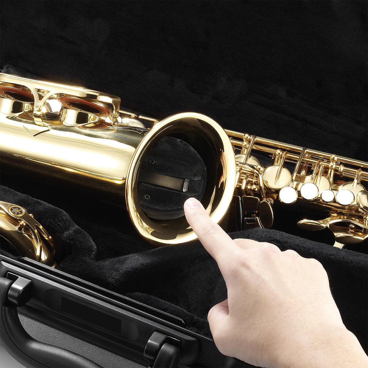 A saxophone in a case with a finger pointing at a folded up stand being store in the bell