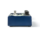 The image shows a guitar effects pedal, likely a distortion or overdrive type, with a dark blue metal housing and an off-white top panel. It features two control knobs on the right, an input/output jack on the left, and a central footswitch button to activate the effect. These pedals modify a guitar's sound and are used on the floor for easy activation during performances or recording.
