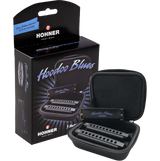The image shows a Hohner "Hoodoo Blues" harmonica set, including a black retail box featuring the logo, "Free Online Lessons!" text, and mention of 3 harmonicas. An open black zippered carrying case displays three harmonicas in different keys for blues playing. Designed for beginners or intermediates, the set is ideal for exploring blues music with convenient portability.