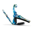 The image shows a Kyser guitar capo with a blue and green swirled, iridescent finish resembling abalone shell. This spring-loaded capo has a curved design and a black rubber pad for clamping securely on the fretboard, allowing guitarists to raise the pitch of all strings at once. Kyser is known for quick-change, functional, and stylish guitar accessories.